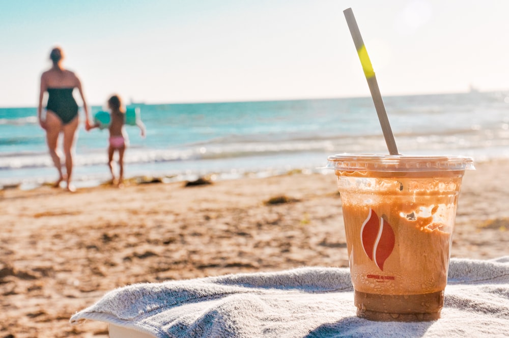 Vaso de plástico transparente con pajita sobre tela blanca en la playa durante el día