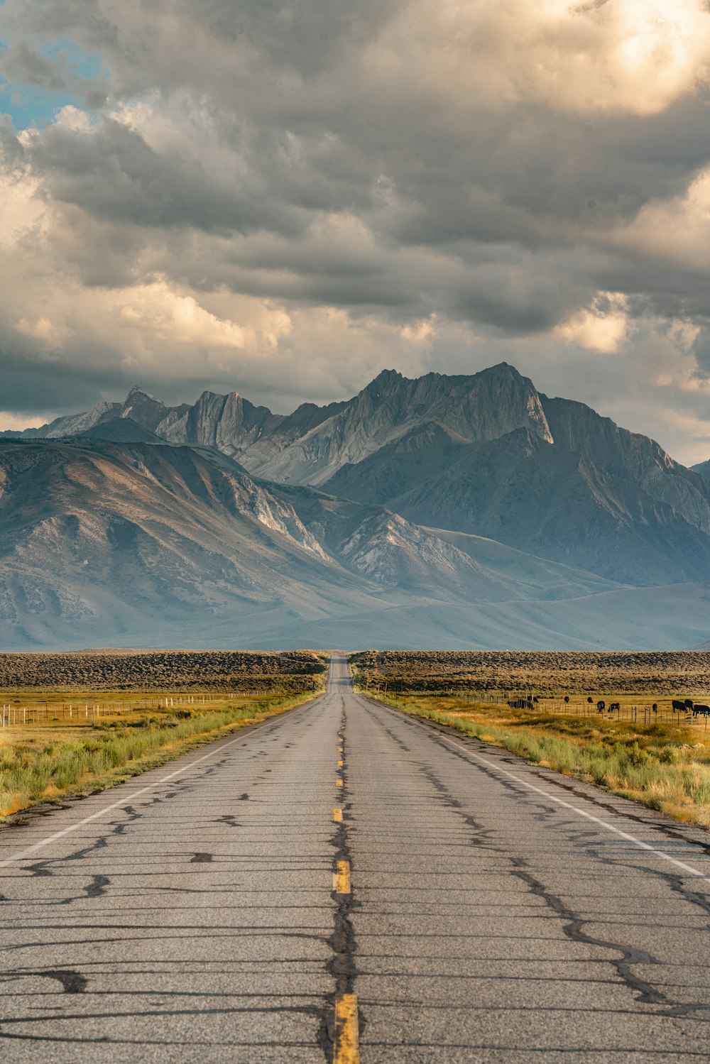 gray concrete road between green grass field near mountain under white clouds during daytime