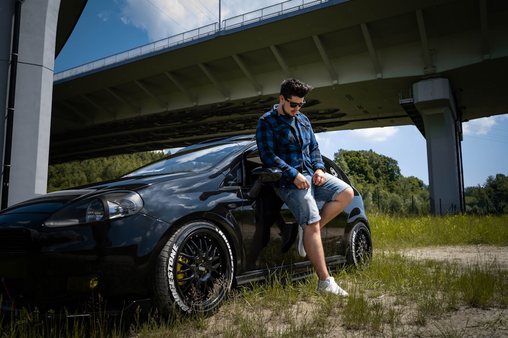 woman in blue and white floral dress shirt and blue denim shorts leaning on black car