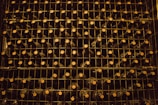 A neatly organized wine rack filled with rows of dark-colored wine bottles, each stacked on metal shelves. The lighting is dim, creating a warm and rustic atmosphere. The caps of the bottles are visible, indicating the bottles are stored horizontally.