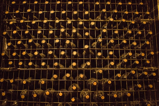 A neatly organized wine rack filled with rows of dark-colored wine bottles, each stacked on metal shelves. The lighting is dim, creating a warm and rustic atmosphere. The caps of the bottles are visible, indicating the bottles are stored horizontally.