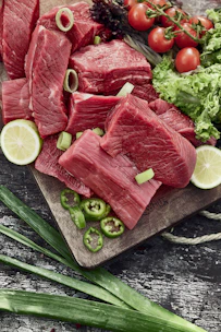 Fresh cuts of meat displayed on a wooden butcher block with vibrant vegetables in the background