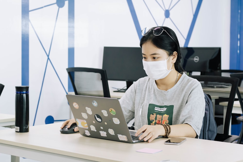 woman in gray crew neck shirt wearing white headphones using macbook