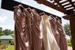 A collection of colorful summer dresses hanging on a rustic wooden rack outdoors.