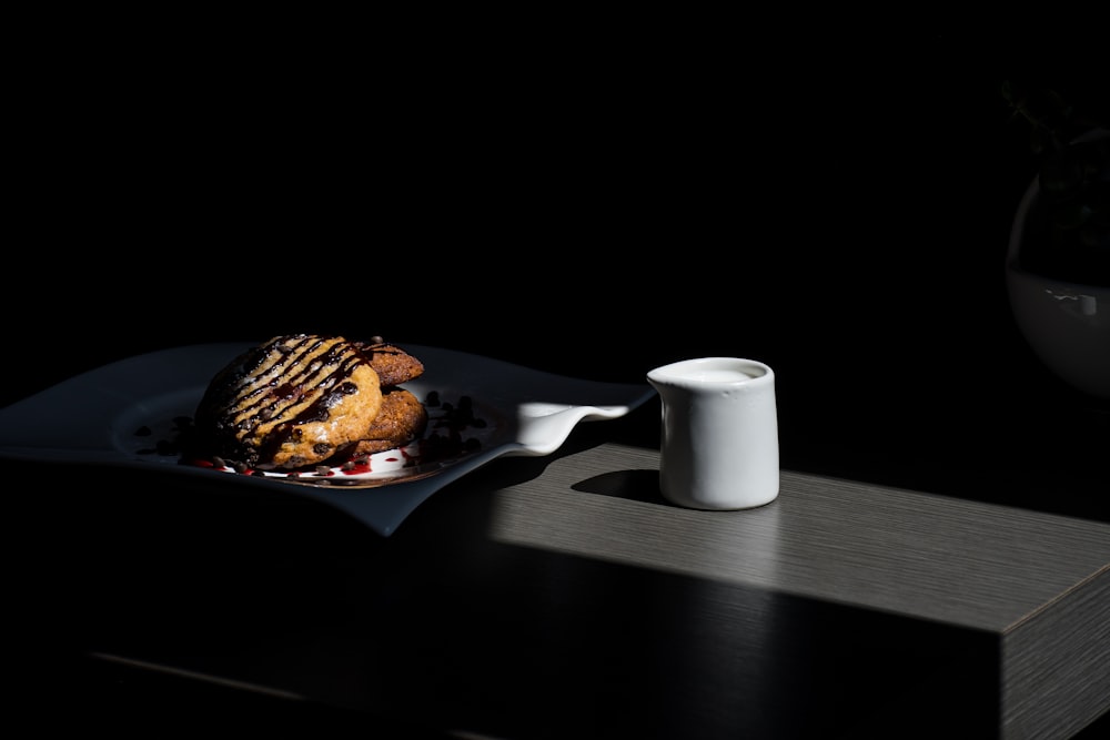 白い陶器の皿の上の茶色のパンの横の白い陶磁器のマグカップ