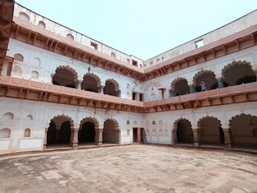 A historical building with arched balconies and stone courtyards. The structure features intricate architectural details, with multiple levels and open corridors. The walls are adorned with decorative elements typical of traditional design.