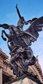 A dramatic bronze statue of a winged horse with a human figure riding it is prominently displayed against a clear blue sky. The sculpture is detailed and dynamic, capturing a sense of movement and mythology.
