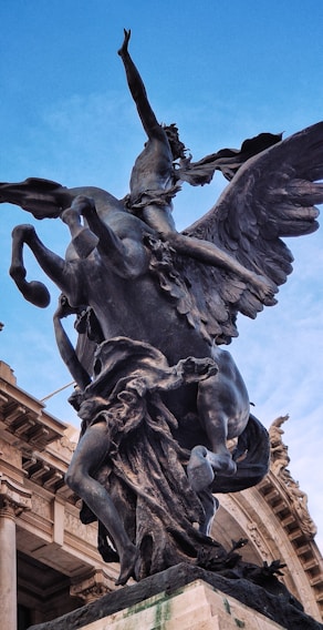 A dramatic bronze statue of a winged horse with a human figure riding it is prominently displayed against a clear blue sky. The sculpture is detailed and dynamic, capturing a sense of movement and mythology.