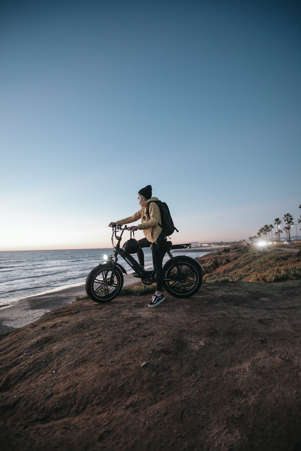 갈색 재킷을 입은 남자가 검은 오토바이를 타고 수역 근처의 갈색 모래 위에