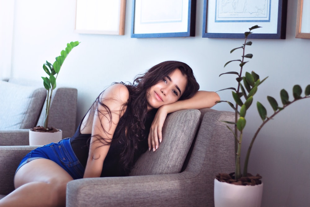 woman in blue tank top and blue denim shorts sitting on gray couch