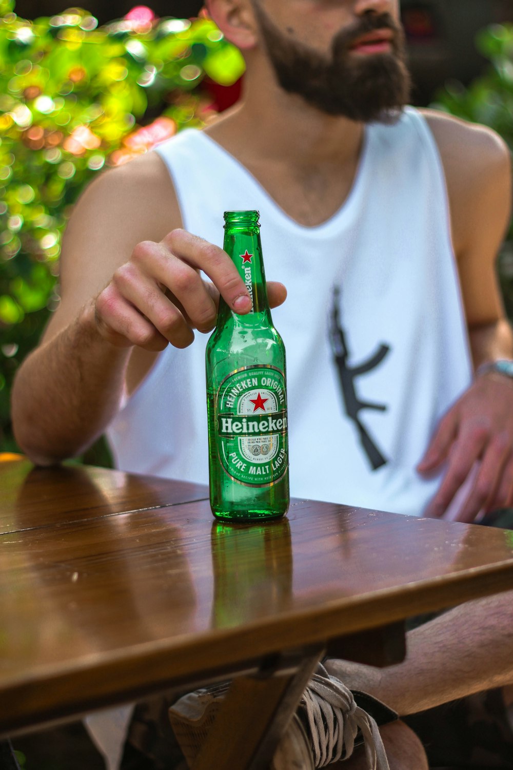 hombre con camiseta blanca sin mangas sosteniendo una botella de vidrio verde