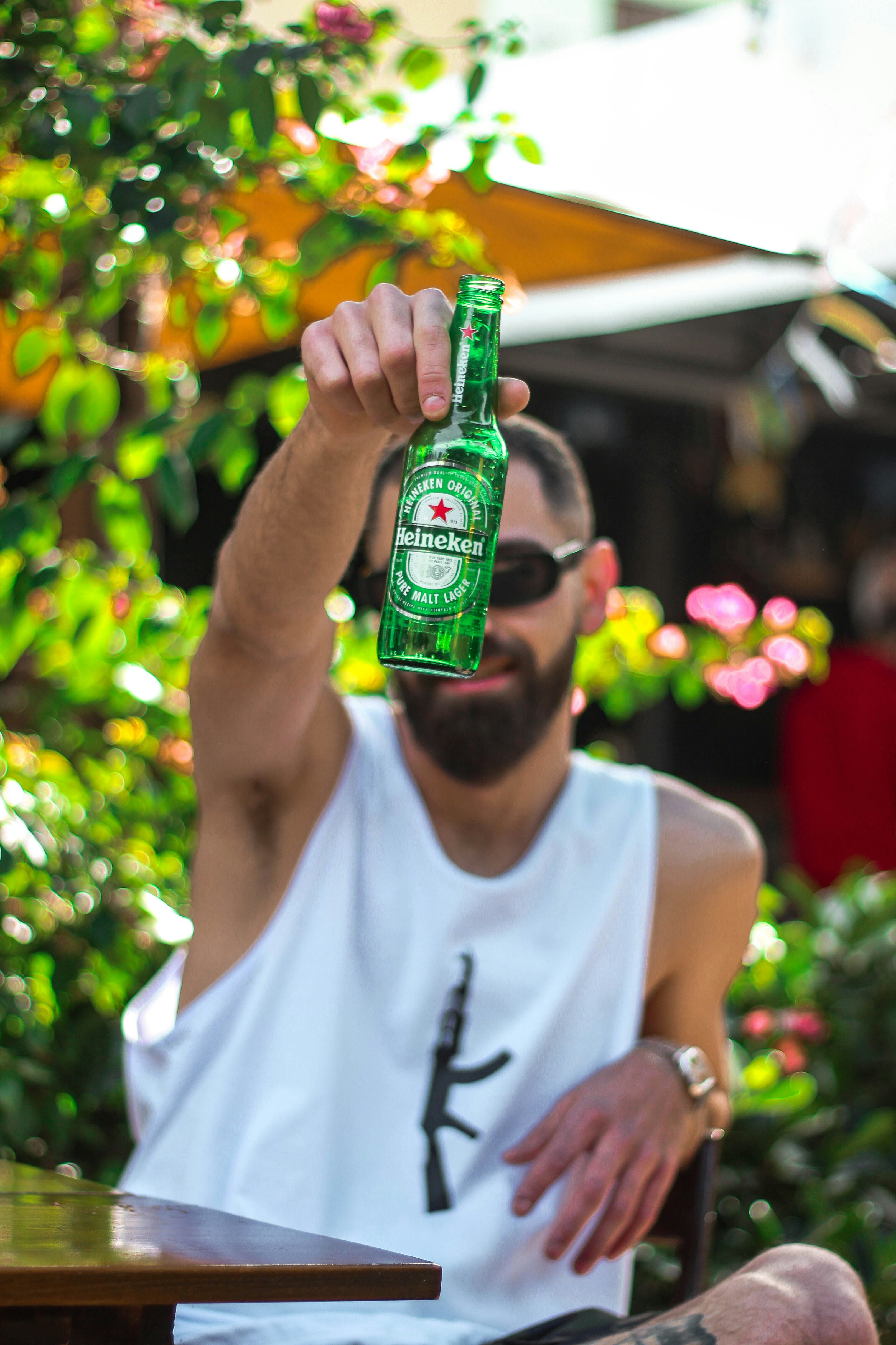man in white tank top holding green glass bottle