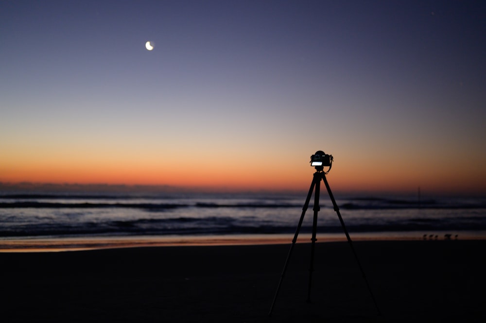 black camera on tripod on beach during sunset