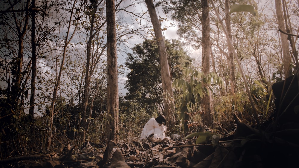 man in white shirt sitting on ground surrounded by trees during daytime