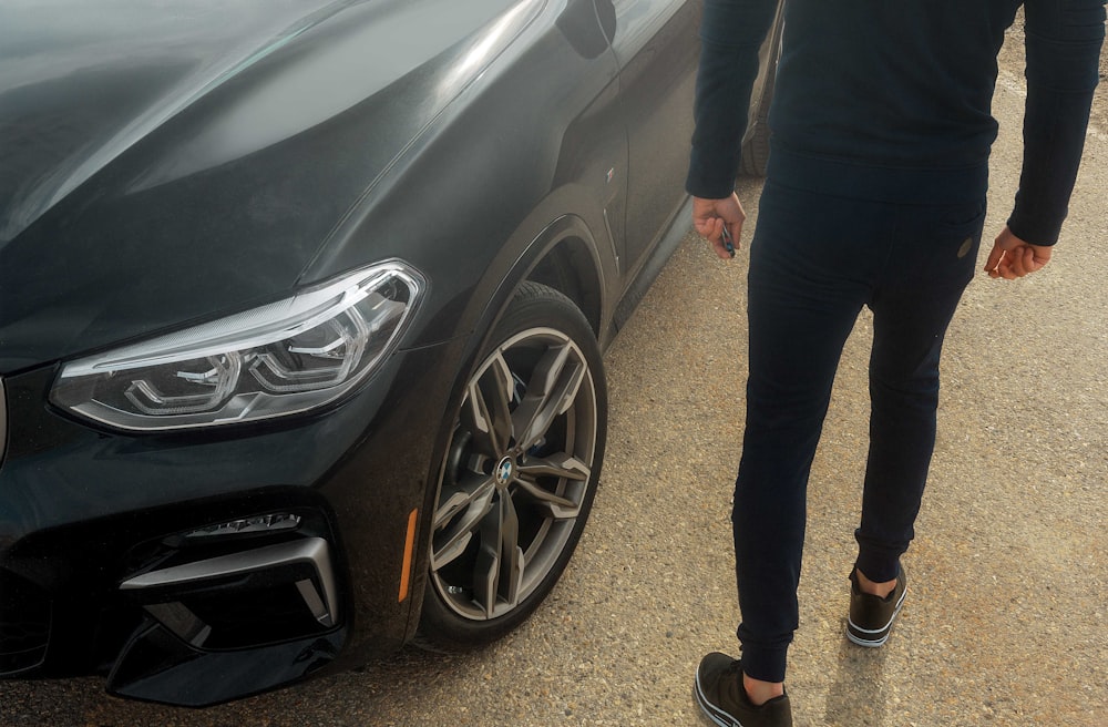 person in black pants and black shoes standing beside black car