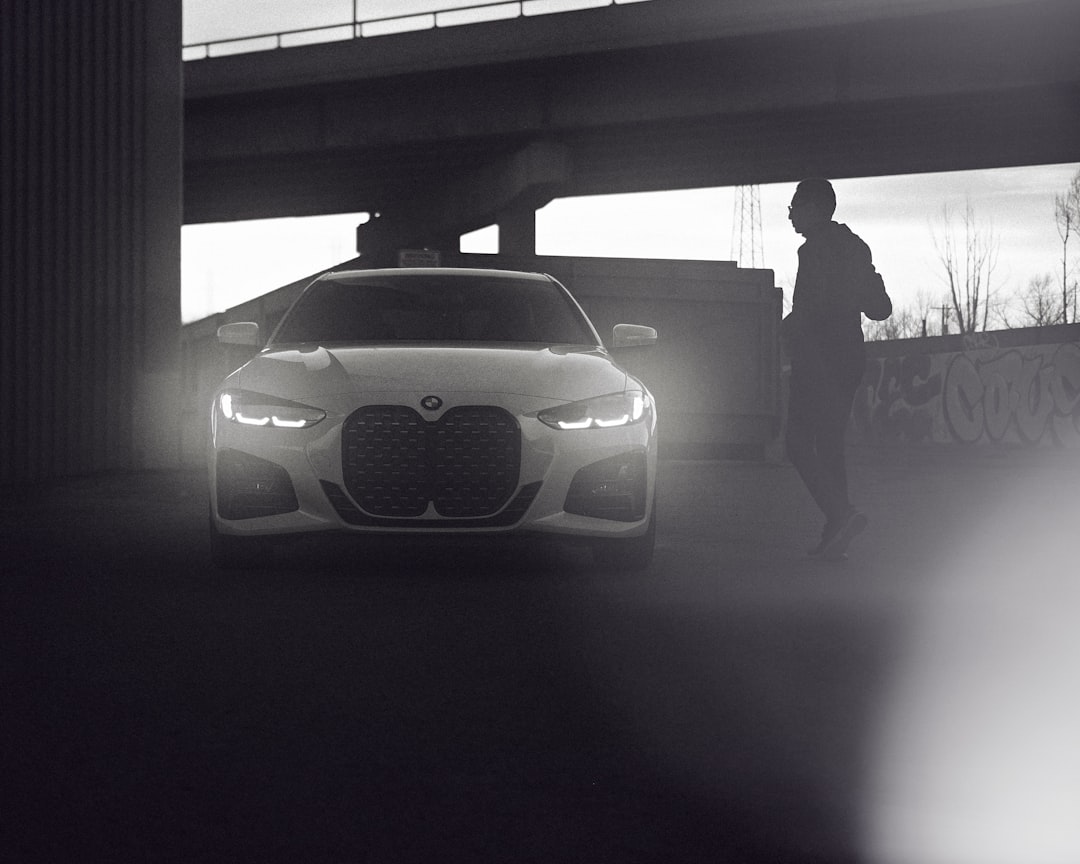 grayscale photo of man standing beside car