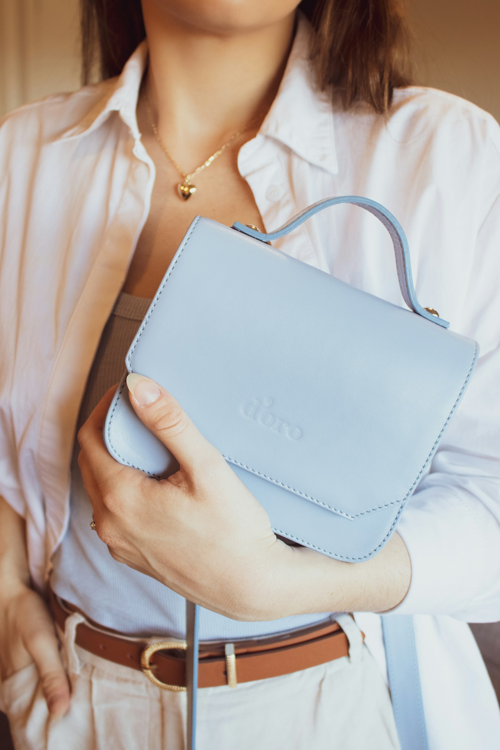 Woman in a white shirt holding a structured white leather handbag