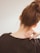 The image depicts the back of a person's head and shoulders, with the individual having brown hair tied up in a messy bun. A hand, with fingers gently curled, is placed on the neck, suggesting a sense of relaxation or relief. The individual is wearing a dark, soft-textured sweater.