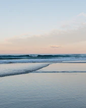 A calm ocean view with soft waves under a pastel blue sky, evoking tranquility.
