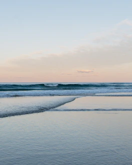 A calm ocean view with soft waves under a pastel blue sky, evoking tranquility.