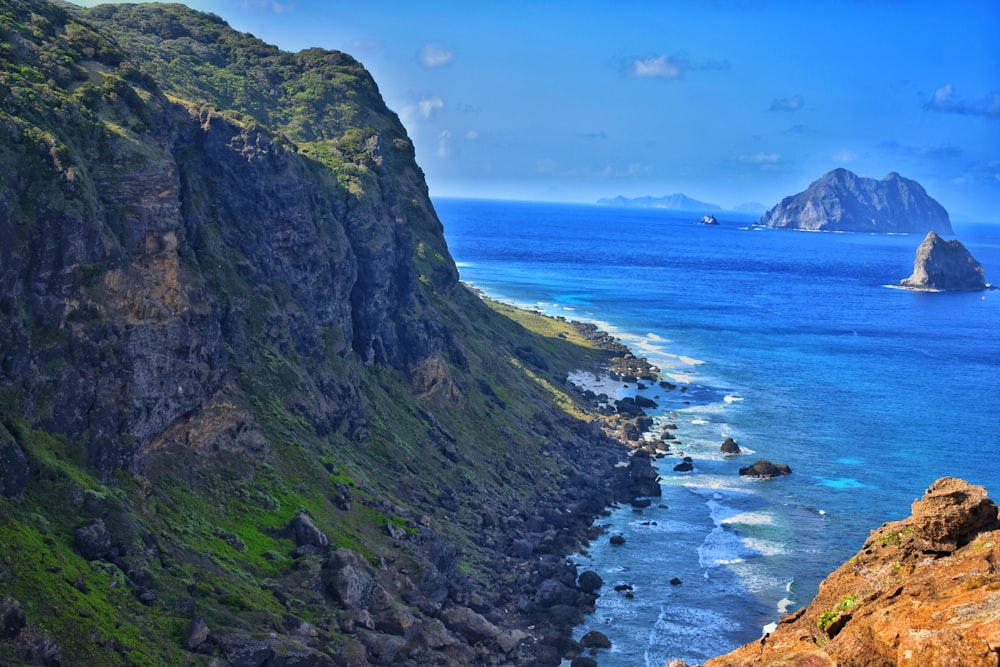 green and brown mountain beside blue sea under blue sky during daytime