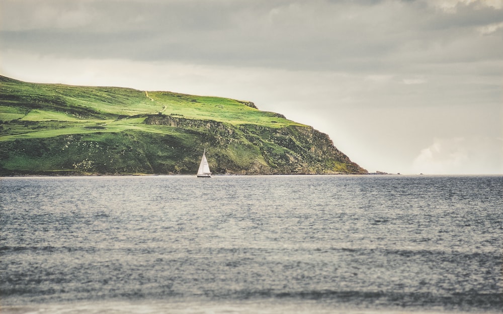 veleiro branco no mar perto da montanha verde sob nuvens brancas durante o dia