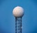 A tall radar tower features a spherical dome with a hexagonal pattern sitting atop a lattice metal structure against a clear blue sky.