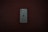 A smartphone with a greenish-gray back and a triple camera system is positioned centrally on a dark wooden surface. The smartphone bears a distinct logo of a partially eaten fruit in the center.