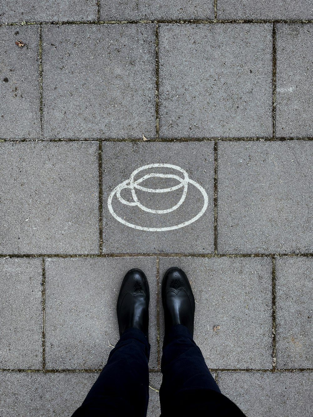 person in black leather shoes standing on gray concrete pavement