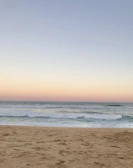 A peaceful beach scene with gentle waves rolling in under a pastel sunset sky.