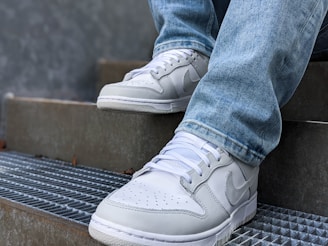 Side view of a man sitting on city steps wearing light-wash Vicky Jeans trousers and sneakers