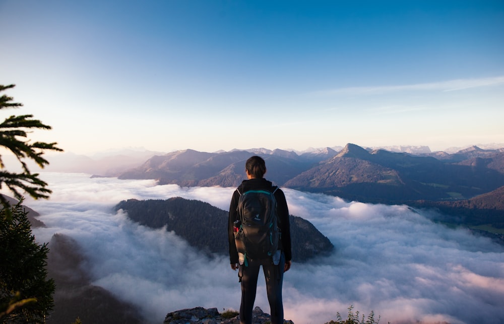 man in black jacket and black pants standing on rock formation looking at the mountains during