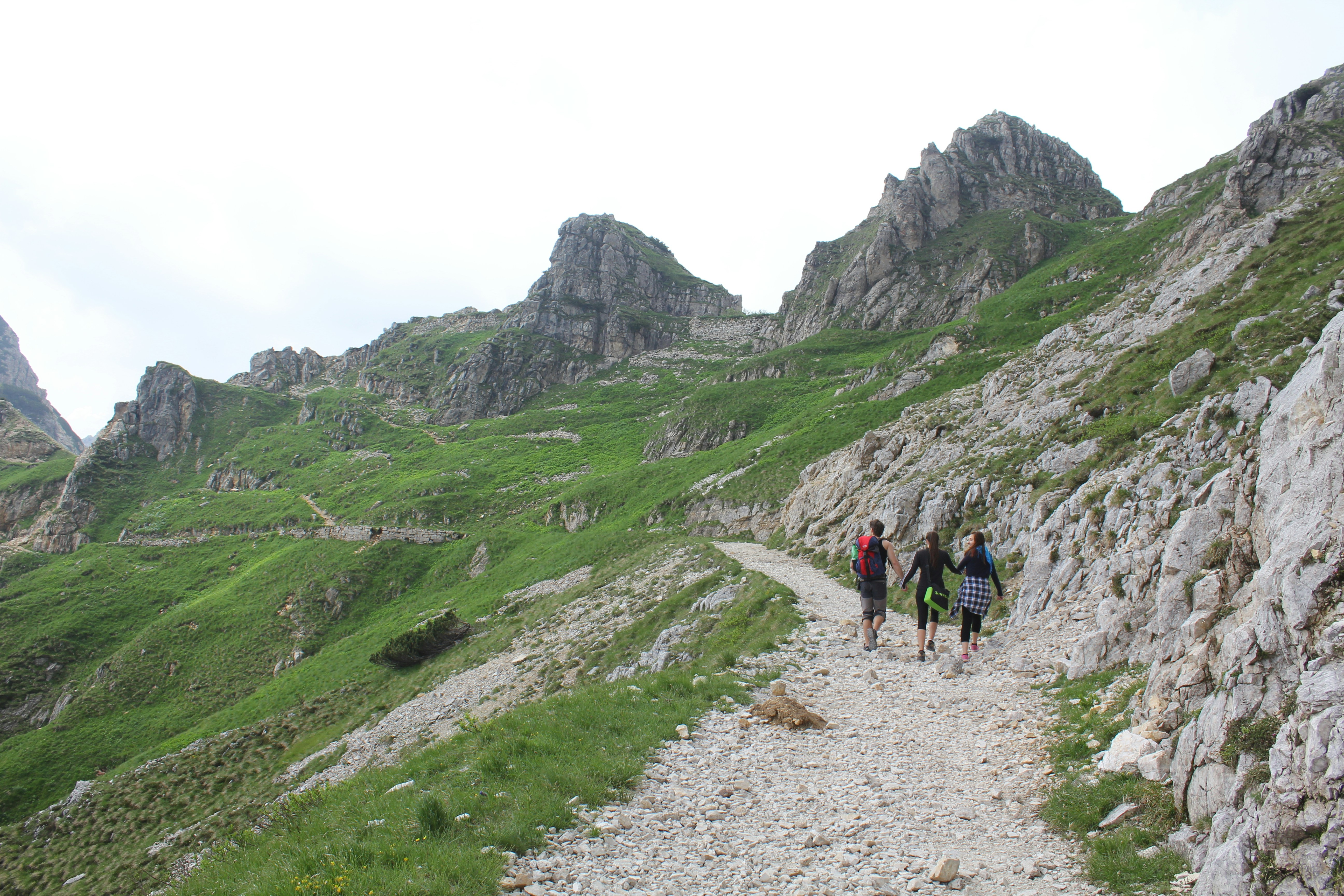 Menschen, die tagsüber auf einem Weg zwischen grünen, mit Gras bedeckten Bergen spazieren gehen