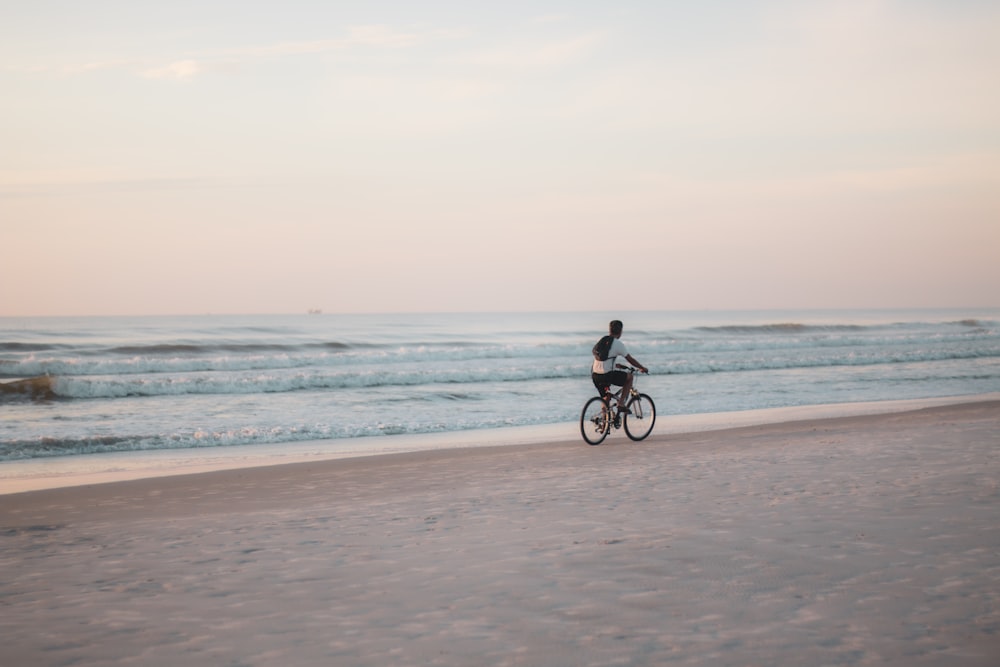 homme en chemise noire faisant du vélo sur la plage pendant la journée