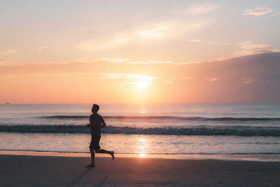 silhouette of man walking on beach during sunset