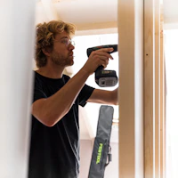 A smiling person using a power drill in a home improvement setting