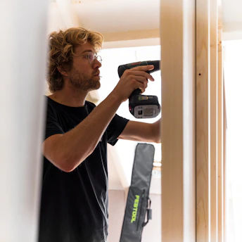 A smiling person using a power drill in a home improvement setting
