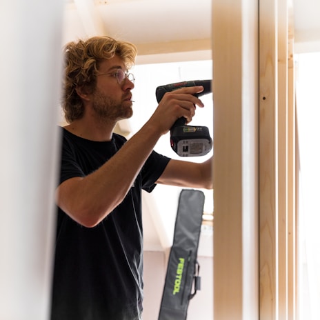 A smiling worker using a drill to install fixtures in a bright room.