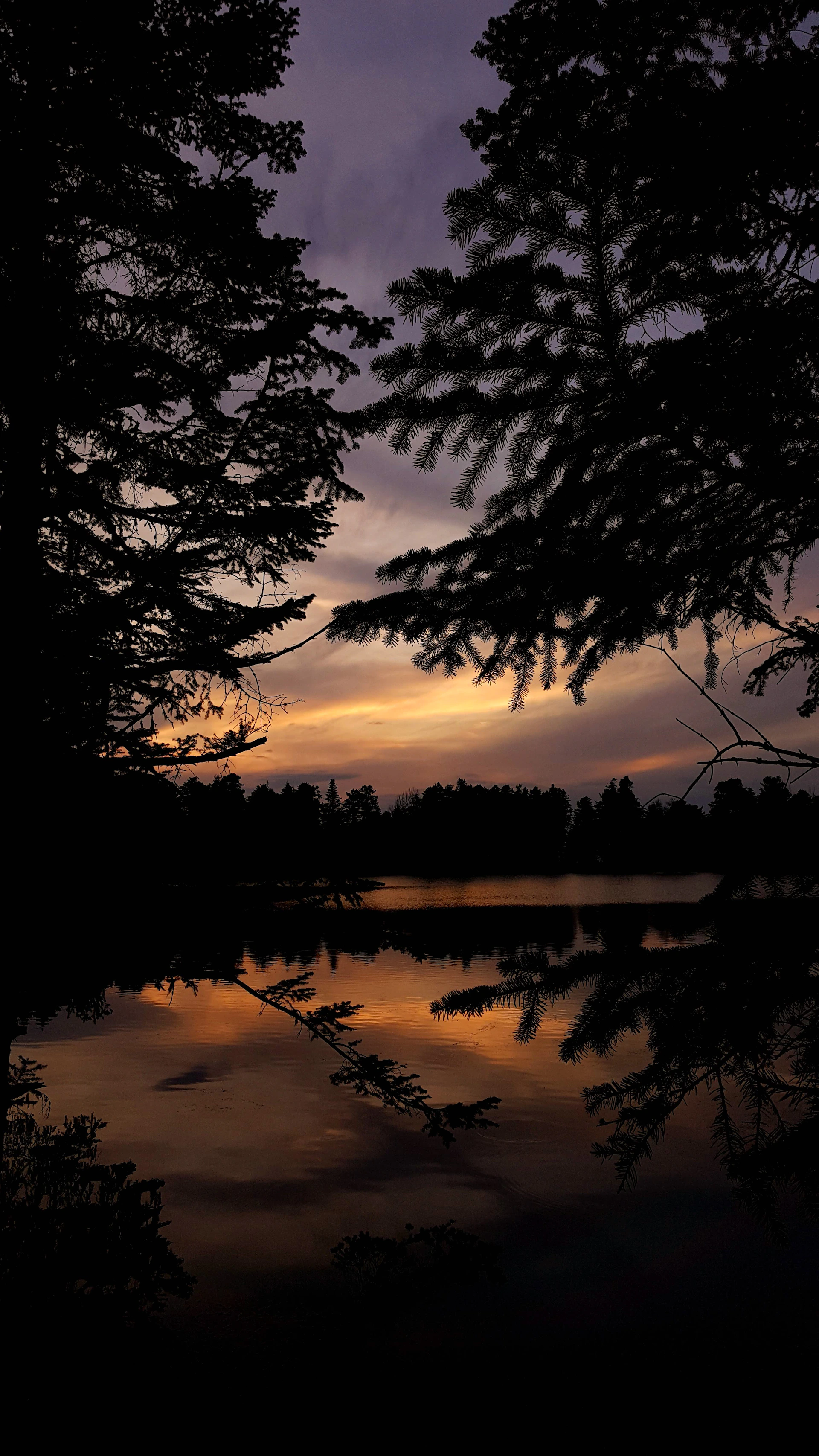 A serene nature scene captured with sharp focus, featuring a calm lake reflecting a colorful sunset sky, evoking peacefulness.