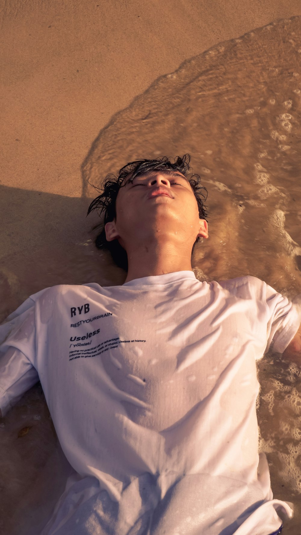 man in white crew neck t-shirt lying on brown sand during daytime