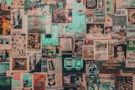 A collage of vintage and contemporary posters and photographs covers a wall. The images include printed art, illustrations, photographs, magazine cut-outs, and handwritten notes. Elements appear layered and overlapping, creating a textured and chaotic visual effect.