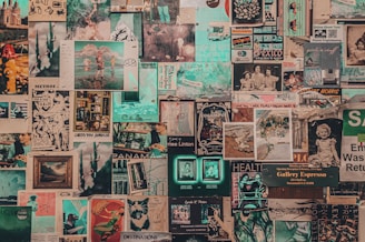 A collage of vintage and contemporary posters and photographs covers a wall. The images include printed art, illustrations, photographs, magazine cut-outs, and handwritten notes. Elements appear layered and overlapping, creating a textured and chaotic visual effect.
