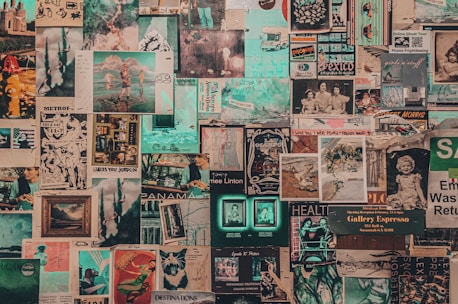 A collage of vintage and contemporary posters and photographs covers a wall. The images include printed art, illustrations, photographs, magazine cut-outs, and handwritten notes. Elements appear layered and overlapping, creating a textured and chaotic visual effect.