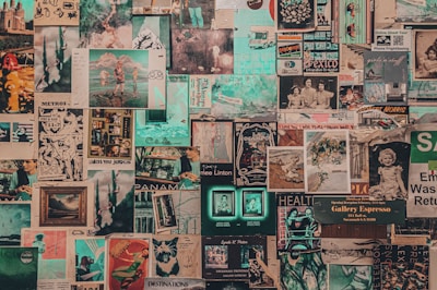 A collage of vintage and contemporary posters and photographs covers a wall. The images include printed art, illustrations, photographs, magazine cut-outs, and handwritten notes. Elements appear layered and overlapping, creating a textured and chaotic visual effect.