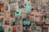 A collage of vintage and contemporary posters and photographs covers a wall. The images include printed art, illustrations, photographs, magazine cut-outs, and handwritten notes. Elements appear layered and overlapping, creating a textured and chaotic visual effect.