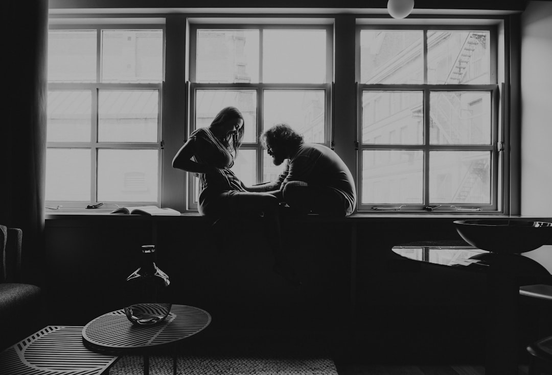 man and woman sitting on chair in grayscale photography