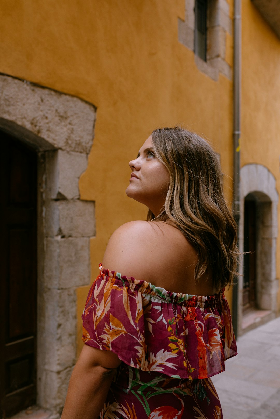 woman in red and blue floral off shoulder dress standing near brown concrete wall during daytime