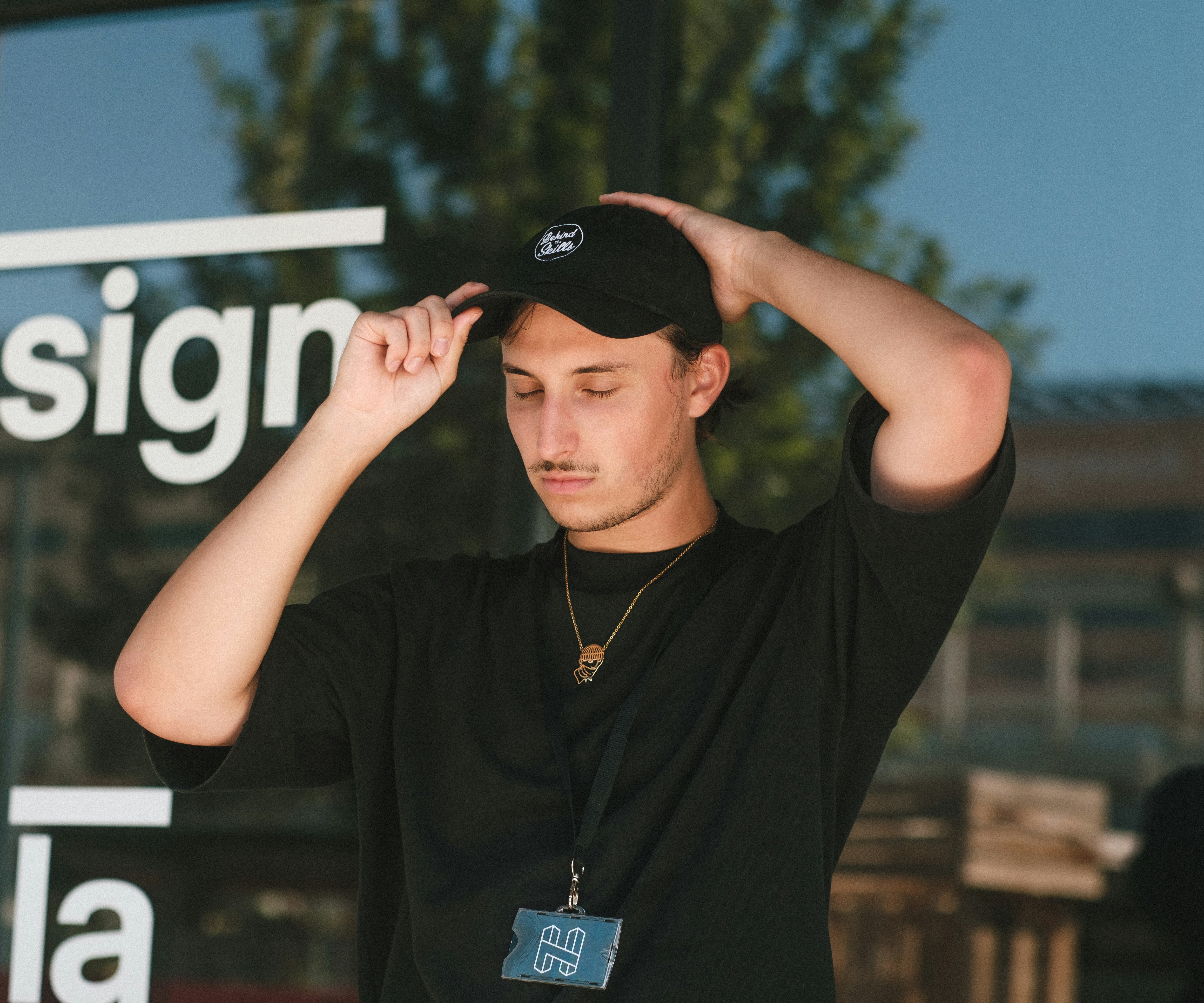 man in black crew neck t-shirt wearing gold necklace and black cap