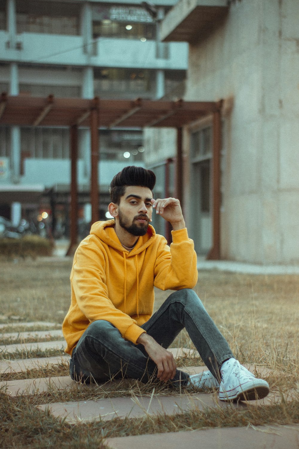 Homme en sweat à capuche jaune et jean bleu assis sur un banc en béton brun pendant la journée