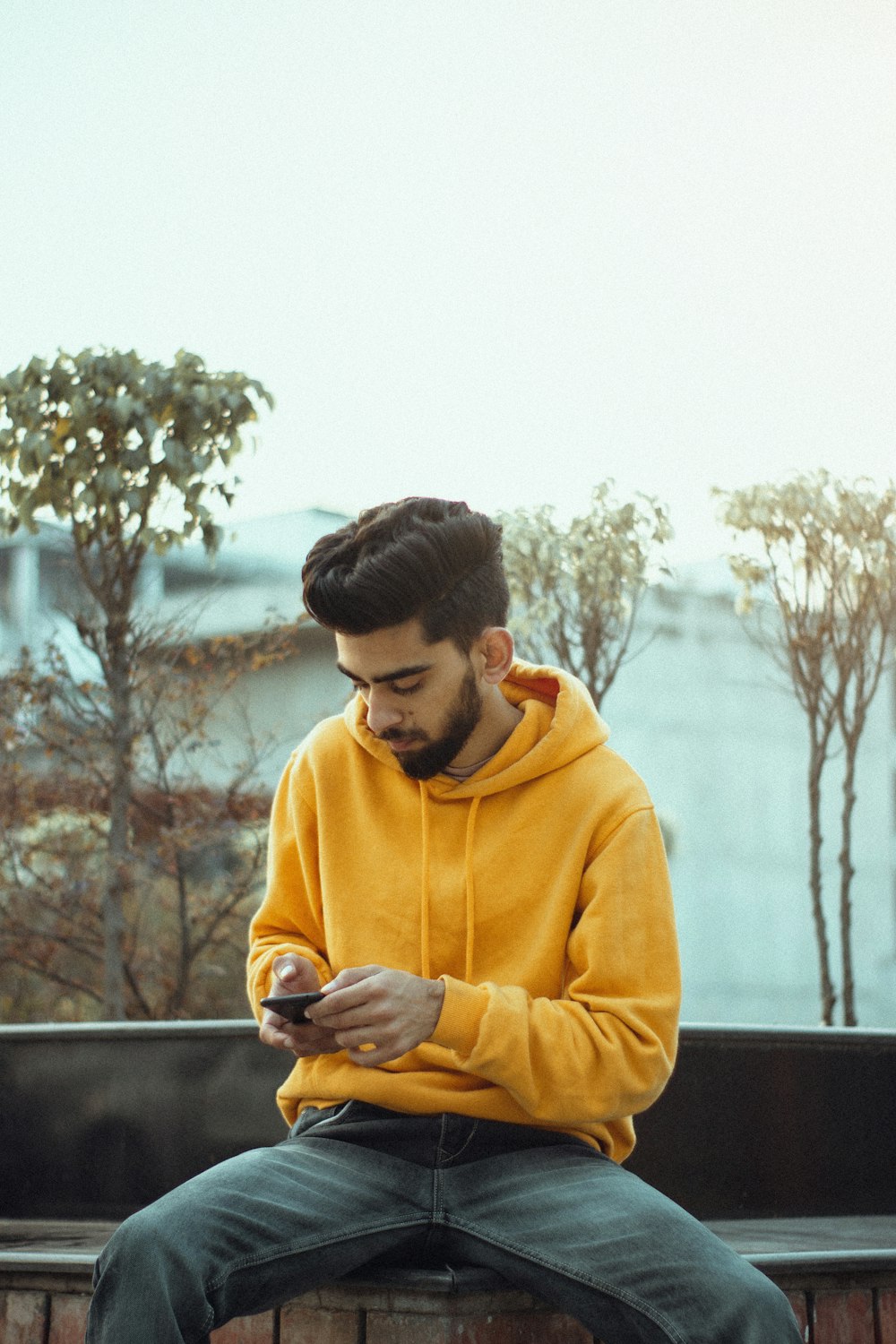 man in yellow hoodie using smartphone